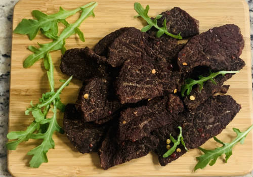 Finished beef jerky piled on a board with green leaves