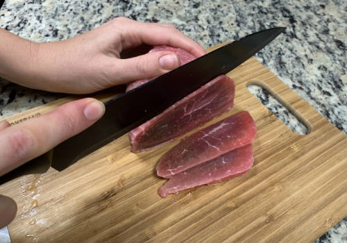 Eye of round being cut into thin slices on a wooden board