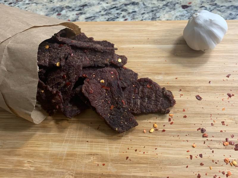 Homemade beef jerky sprinkled with red pepper flakes on a cutting board