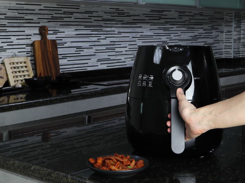 A hand holding the handle of a black countertop air fryer
