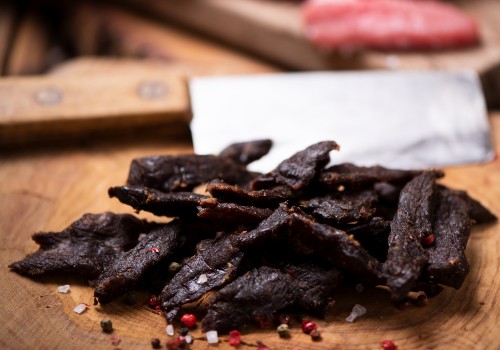 Beef jerky pieces on a wooden board beside a cleaver