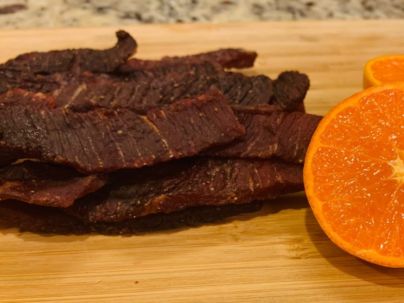 Brown sugar beef jerky strips beside a halved orange