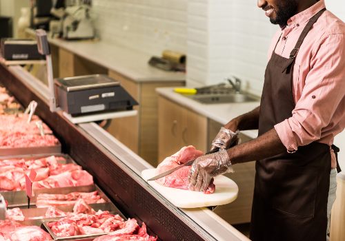A butcher weighing a cut of beef at the meat counter