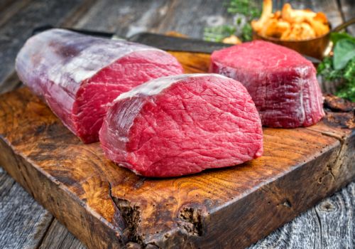 Raw beef roast and thick slices on a wooden board