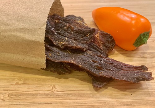 Beef jerky spilling from a paper bag beside a habanero