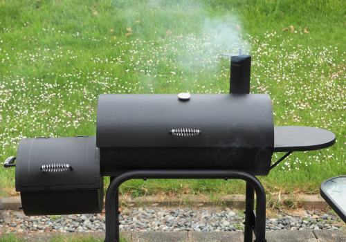 A black offset smoker with a side firebox releasing smoke