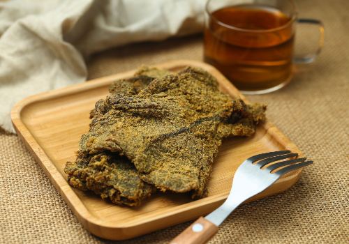 Seasoned snack strips on a wooden plate beside a drink