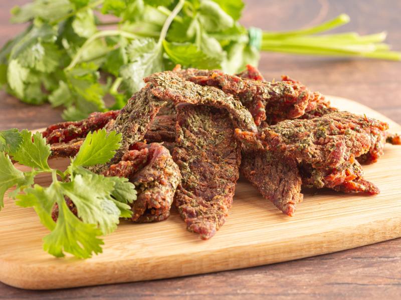 Herb-coated jerky strips on a board with cilantro