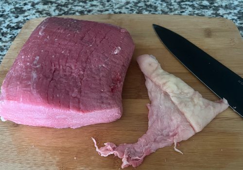 A trimmed roast beside a removed strip of fat and a knife