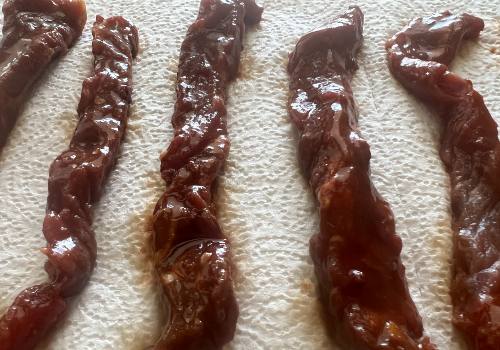 Glossy marinated beef strips draining on paper towels