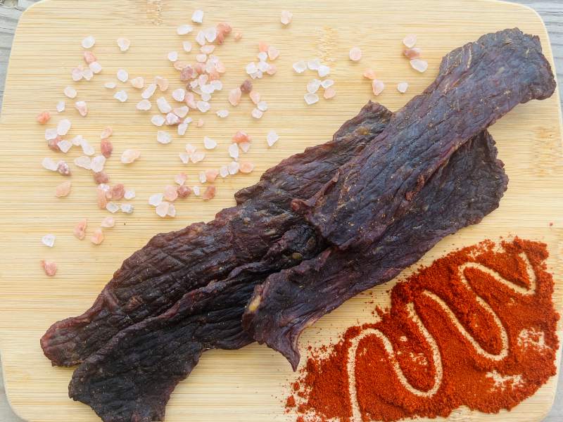 Long barbecue jerky strips beside salt and red seasoning