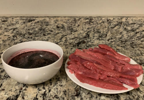 A bowl of dark marinade beside sliced raw beef