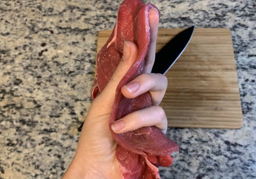 A hand holding thin slices of raw sirloin tip