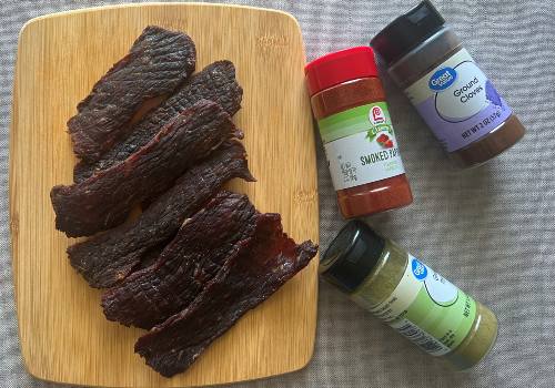 Homemade beef jerky beside jars of spices