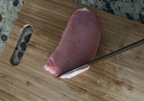 A knife removing an edge of fat from a pork chop