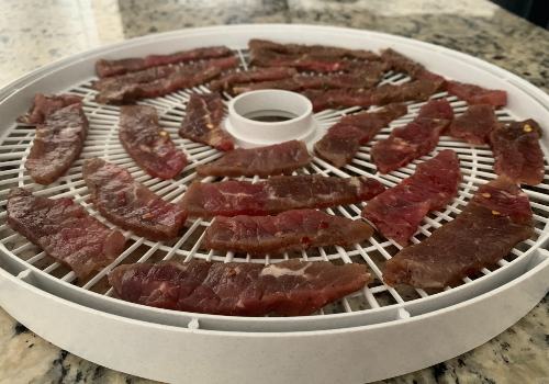 Honey-peppered beef strips on a white dehydrator tray