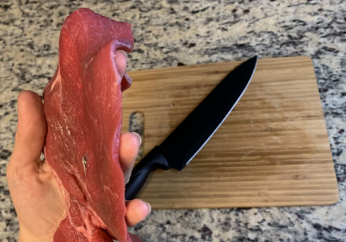A hand holding thin raw sirloin tip slices