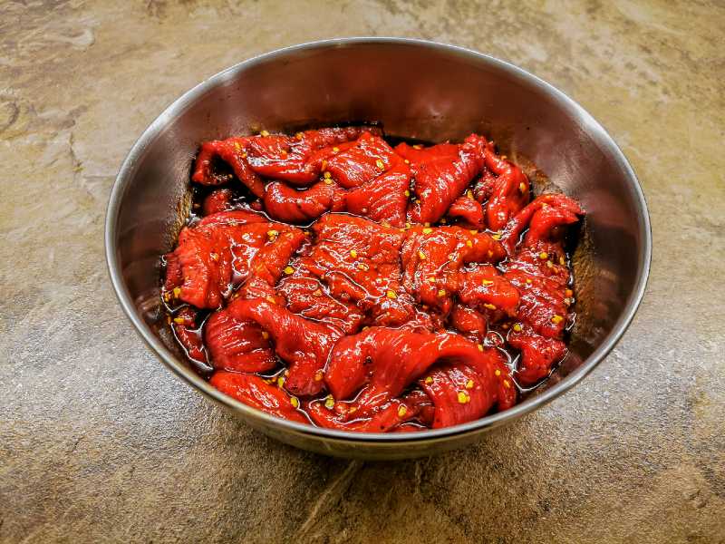 Marinated meat strips in a stainless steel bowl