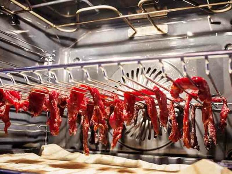 Thin meat strips hanging from a rack inside an oven