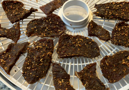 Pepper-coated jerky pieces on a round dehydrator tray