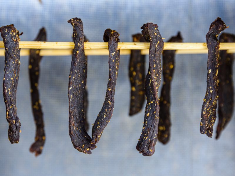 Long dried meat strips hanging from a horizontal rod