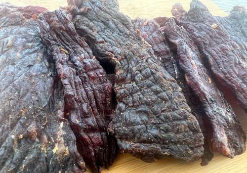 Thick dark jerky pieces arranged on a cutting board