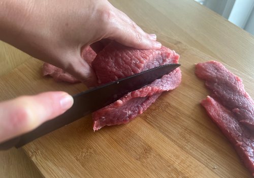 A knife slicing beef into short strips