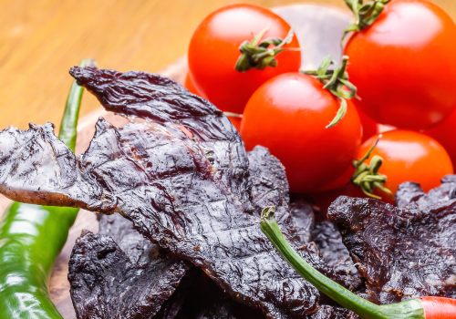 Dark jerky strips beside tomatoes and greens