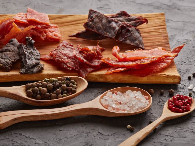 Assorted dried meat pieces with spoons of salt and peppercorns