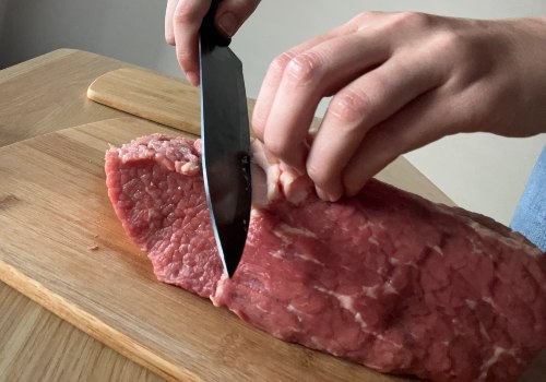 A knife trimming the outside of a raw beef roast