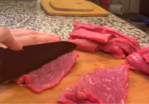 A cook slicing beef into long strips
