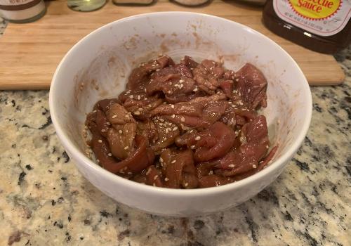 Sesame-speckled beef strips being mixed in a white bowl