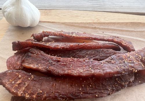 Long jerky strips beside a garlic bulb on a board