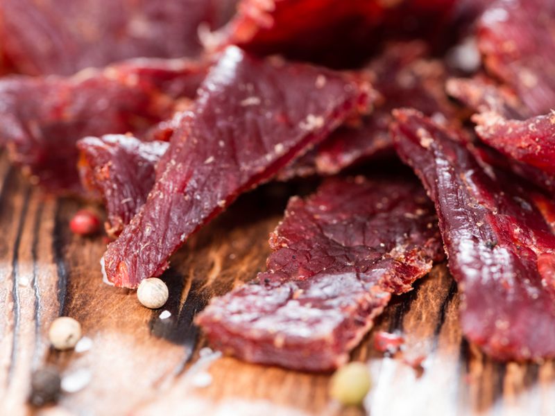 Close-up of dark red beef jerky strips with seasoning