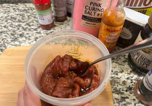 Beef strips being mixed with dark marinade in a plastic container