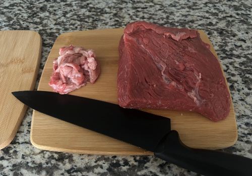 Trimmed bottom round beef beside a knife and removed fat