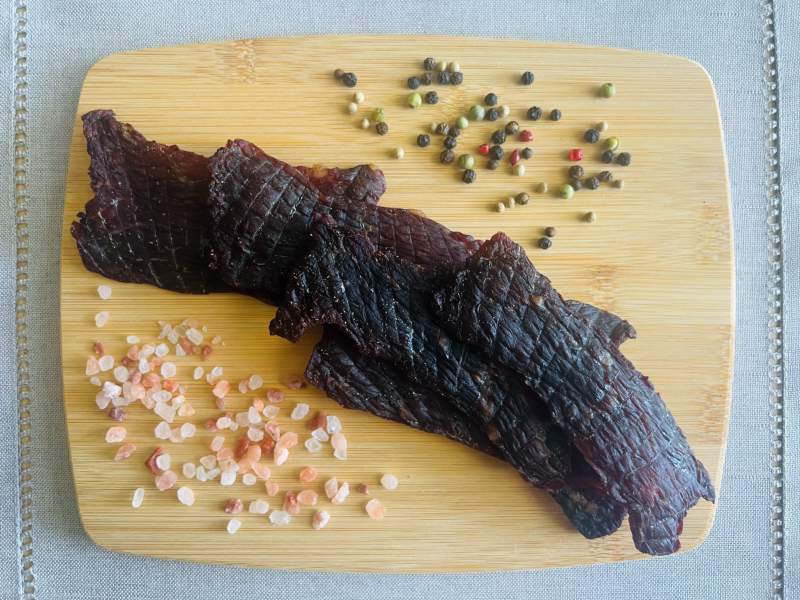 Dark jerky strips beside salt crystals and peppercorns