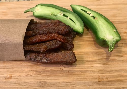 Spicy salmon jerky stacked beside cut green peppers