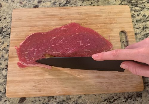 A knife trimming the edge of a thin beef slice
