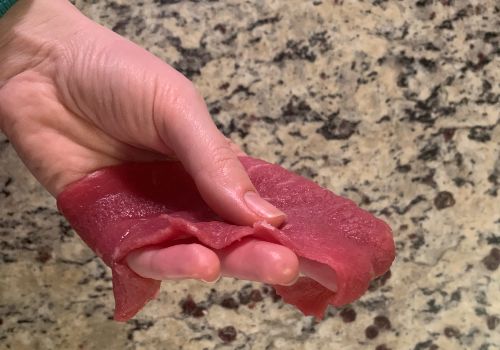 A hand holding a thin raw beef slice