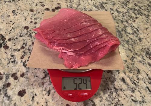Thin raw beef slices on a scale reading 524 grams