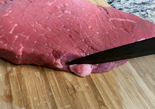 Knife trimming a small strip of fat from raw beef