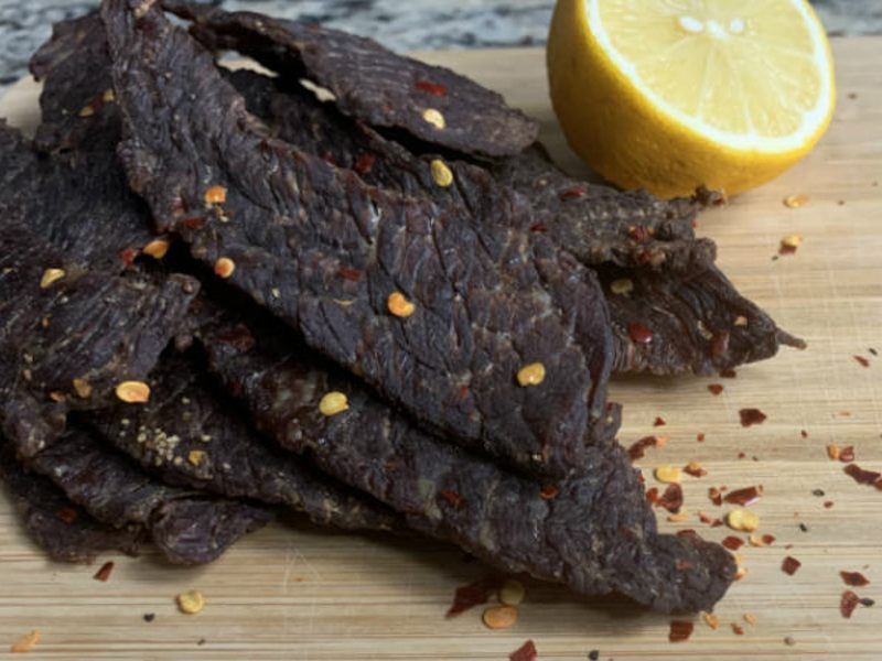Dark beef jerky scattered with pepper flakes beside a lemon half