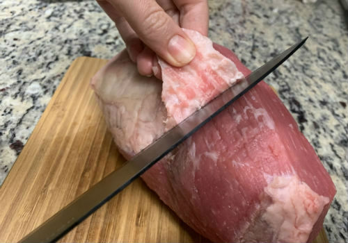 Hands trimming a layer of fat from eye of round beef