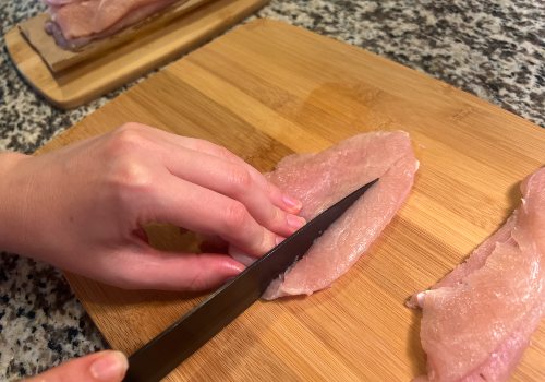 Knife cutting a turkey cutlet into strips