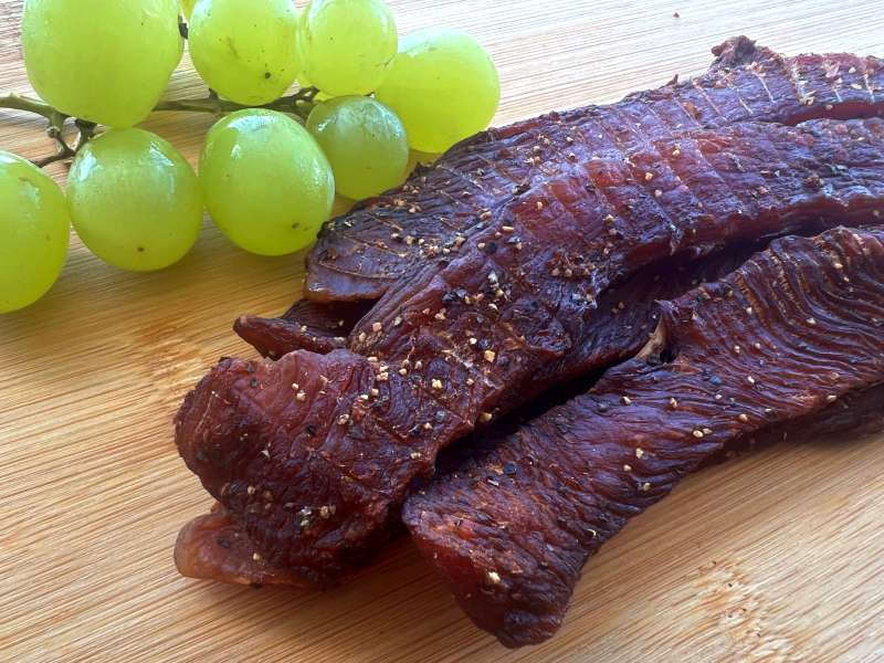 Dark turkey jerky strips beside green grapes