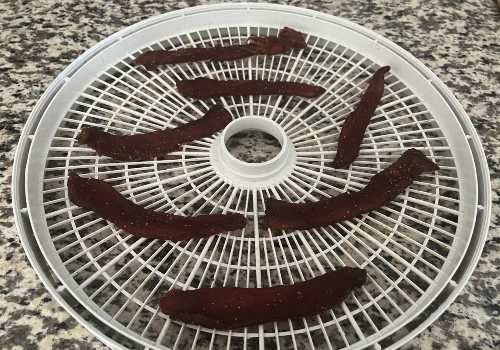 Dark turkey jerky strips on a dehydrator tray