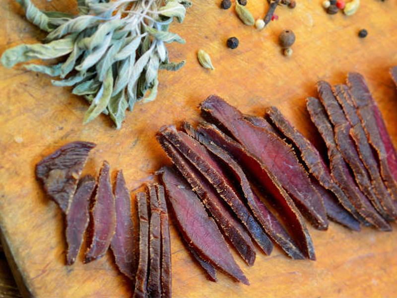 Thin strips of dried meat on a board with herbs and peppercorns