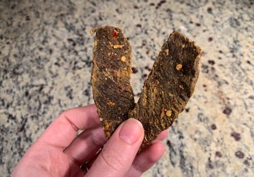 Hand holding two pieces of dried beef jerky