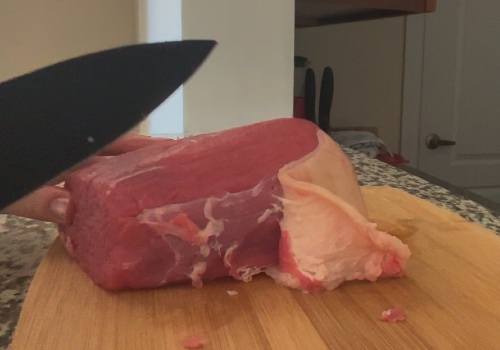 Knife trimming a layer of fat from raw beef